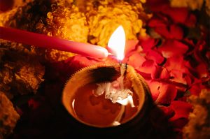 a small red candle lights a larger candle in a small pot.