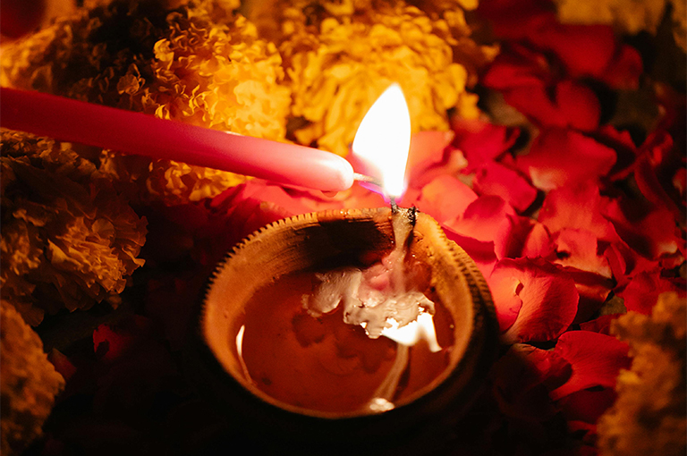 a small red candle lights a larger candle in a small pot.